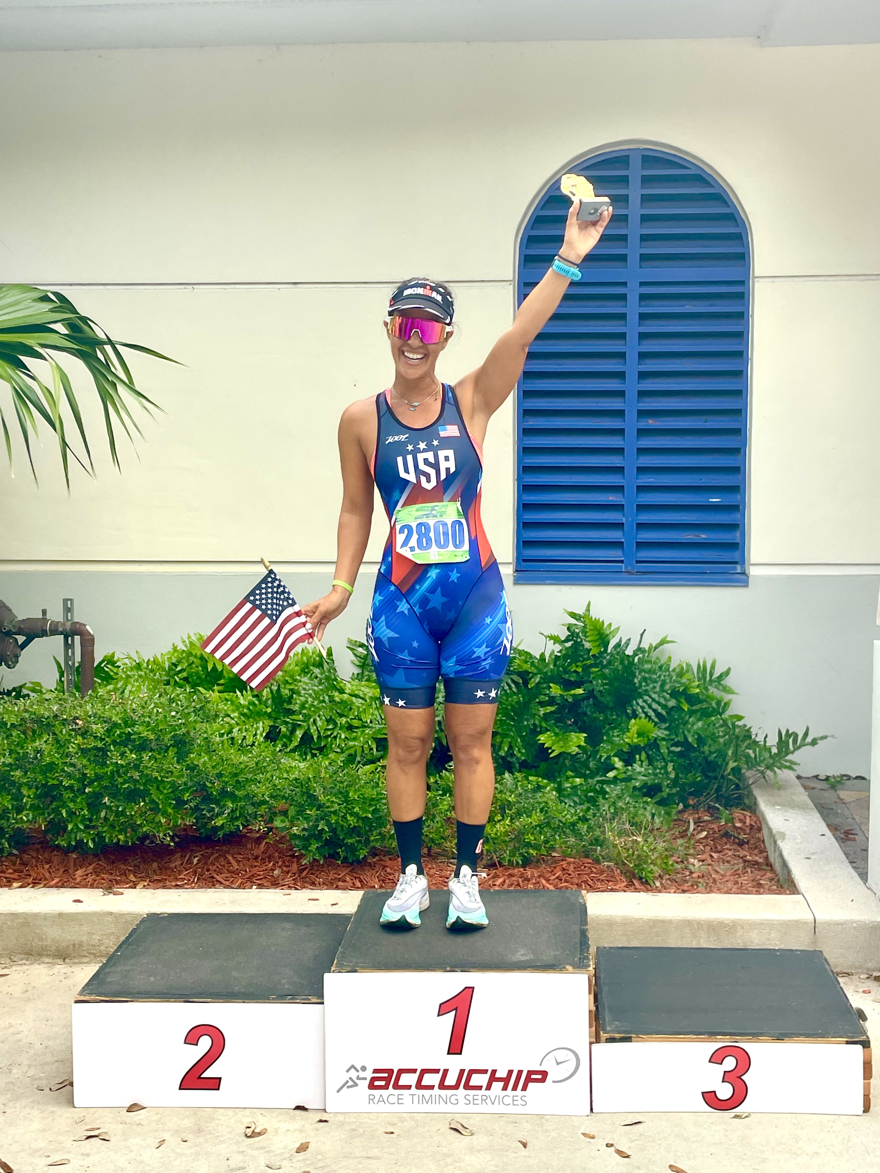 Dr. Hadar on the first-place podium in Team USA tri kit holding an American flag